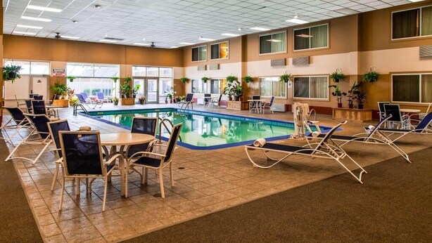 An indoor swimming pool with lounge chairs and tables, surrounded by windows and potted plants. - Rock Island Inn & Suites Marshalltown (Marshalltown)