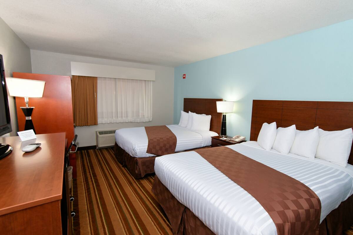 A hotel room with two beds, a desk with a lamp, a telephone, and a window with curtains.