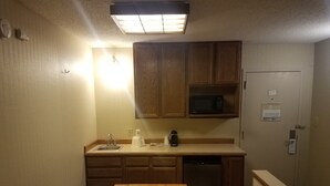 A compact kitchen with wooden cabinets, a microwave, a sink, and a dishwasher. - Rock Island Inn & Suites Marshalltown (Marshalltown)