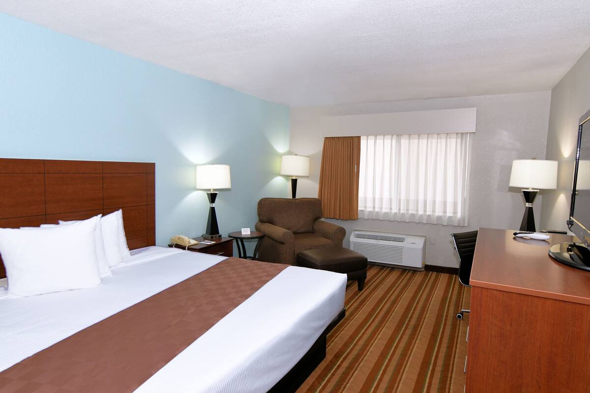 A hotel room with a large bed, a desk, a chair, and a window with curtains.