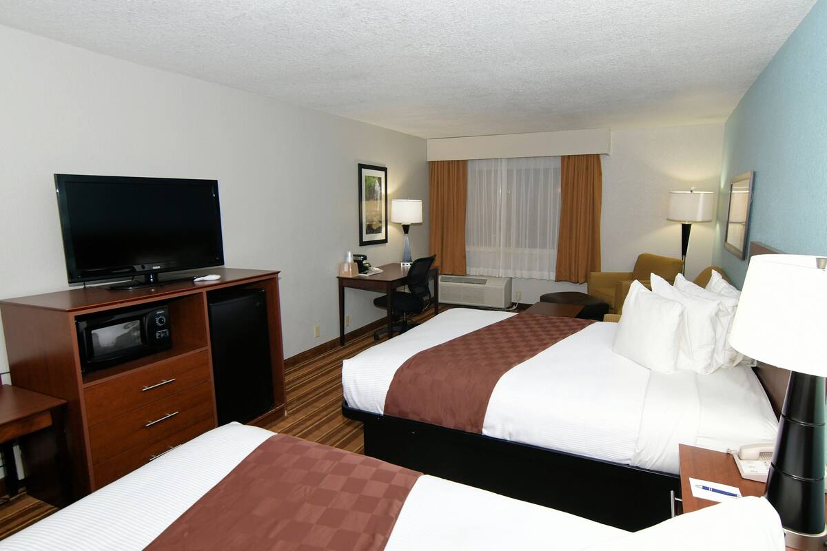 A hotel room with two beds, a desk, a television, a desk lamp, and a window with curtains.