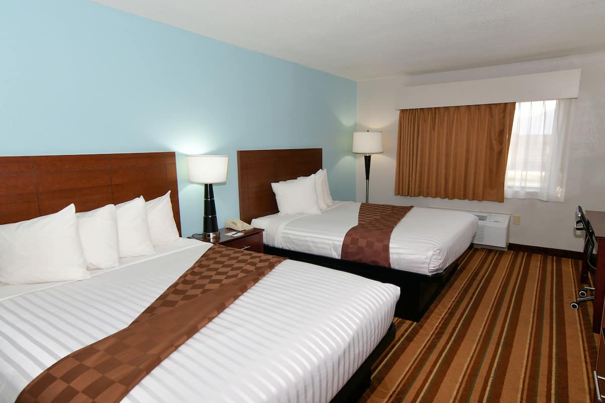 A hotel room with two beds, a nightstand, a lamp, and a window with curtains.