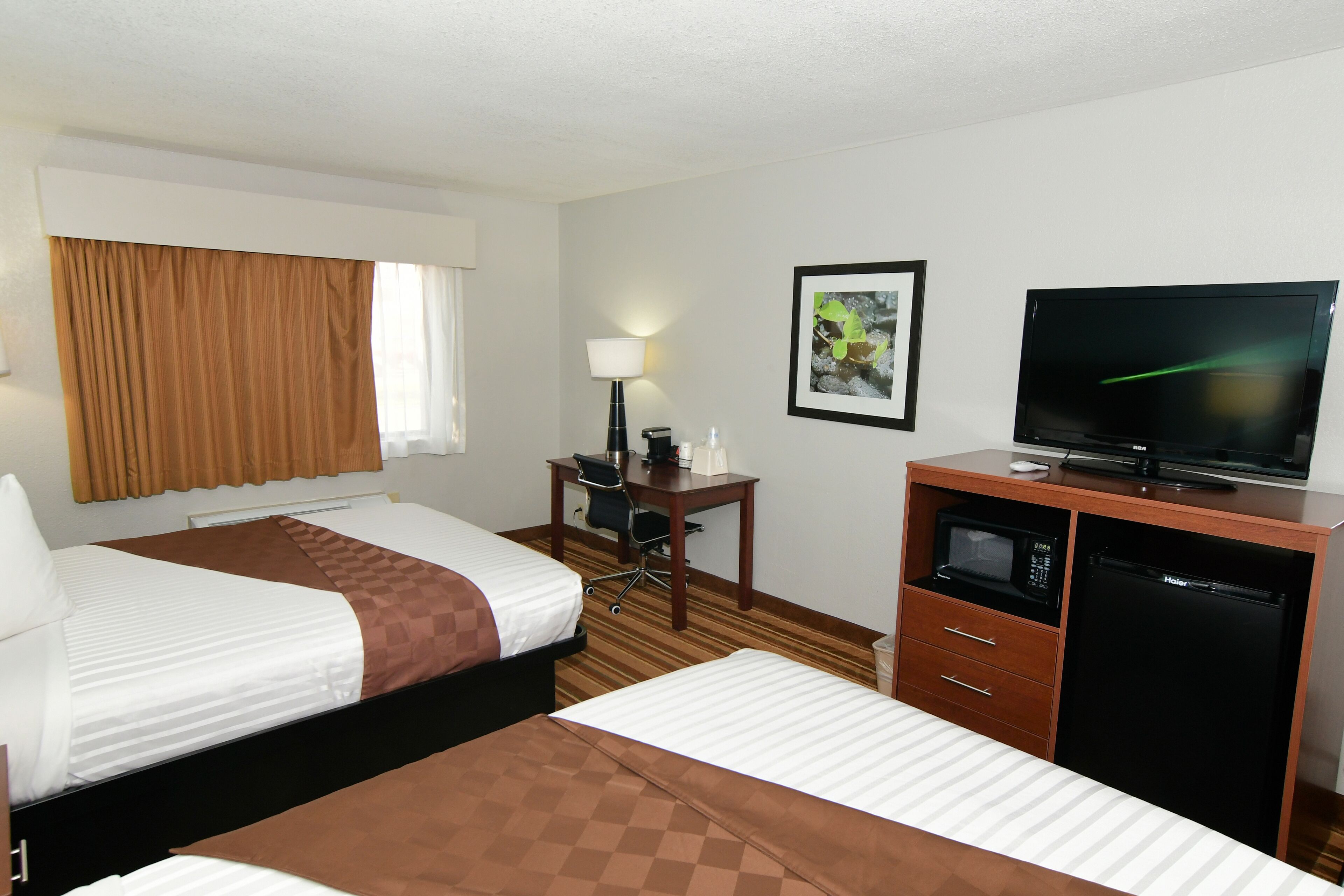 Habitación de hotel con dos camas, un escritorio con silla, televisor, microondas y refrigerador.