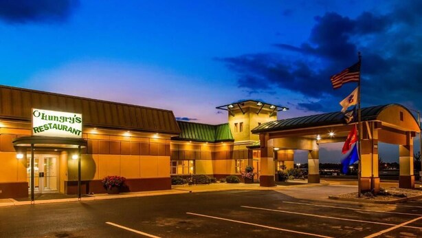 A hotel with a restaurant named "Hungry's Restaurant" at its entrance, featuring a covered parking area and a flagpole with flags.