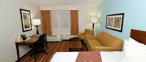 Habitación de hotel con cama, escritorio con silla, sofá, una mesita, lámpara y ventana con cortinas.