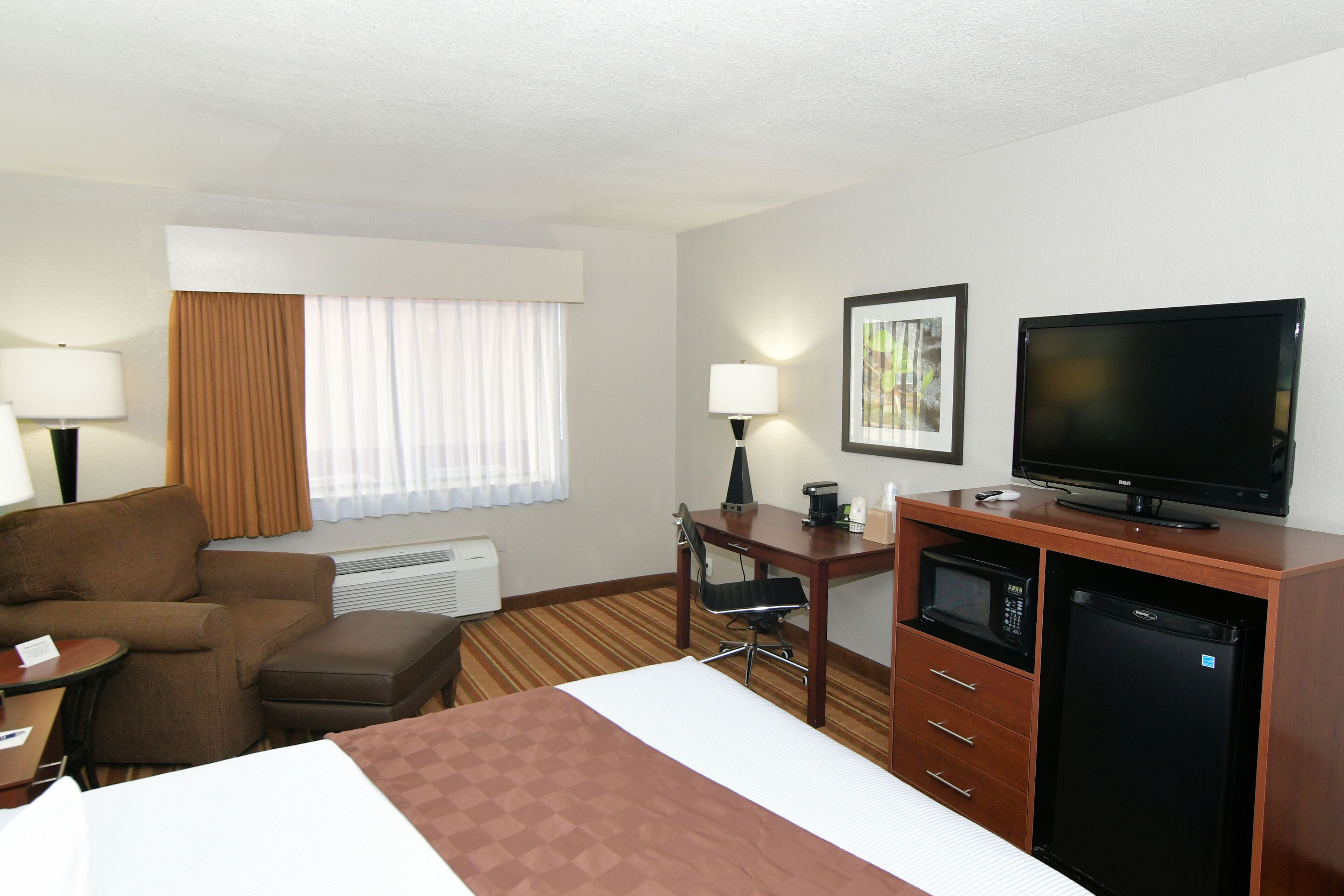 A hotel room with a bed, a desk with a computer, a television, a microwave, and a refrigerator.