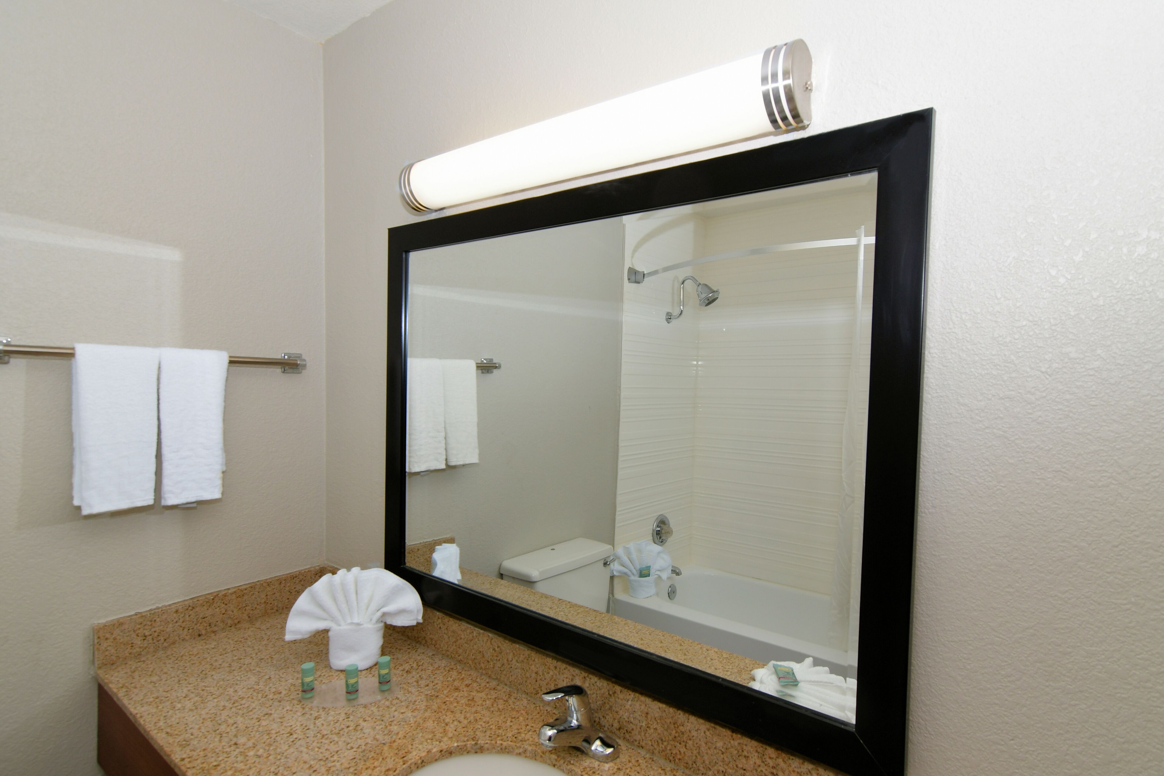 A bathroom with a large mirror, a sink, a towel rack, and a shower.