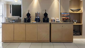Una moderna zona de recepción de hotel con un mostrador de madera, máquinas de café y una exposición de frutas.