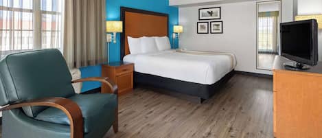 Habitación de hotel con cama, escritorio, silla, televisor y ventana con cortinas.