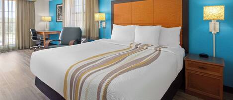 A hotel room with a large bed, a desk, a chair, and a nightstand.