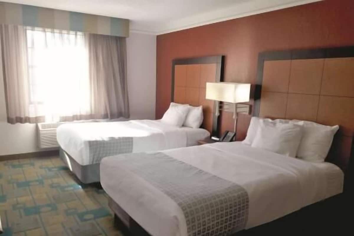 Une chambre d’hôtel avec deux lits, une table de chevet, une lampe et une fenêtre avec des rideaux.