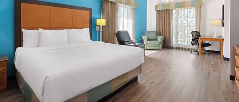 Quarto de hotel com uma cama grande, uma escrivaninha com cadeira, uma poltrona pequena e um ventilador de teto.