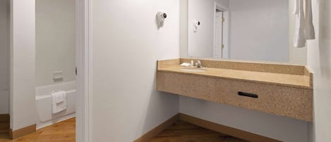 Une salle de bain moderne avec un comptoir en granit, un grand miroir et une zone de douche visible au fond.