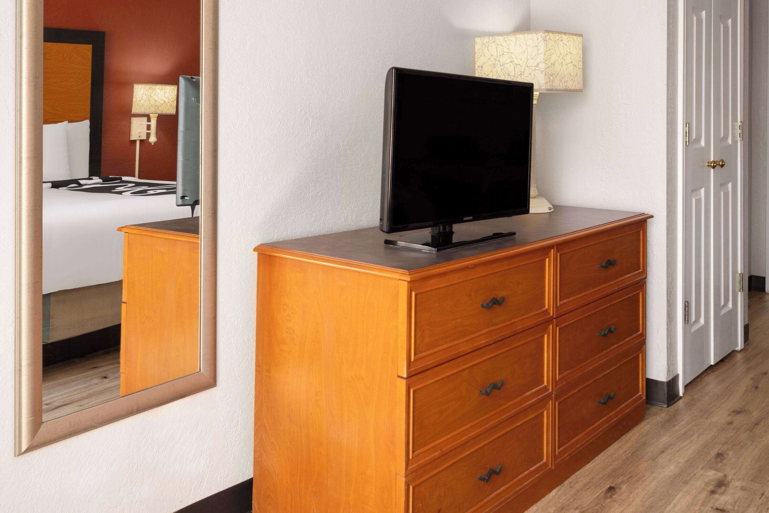 A hotel room with a wooden dresser, a flat-screen TV, and a lamp.
