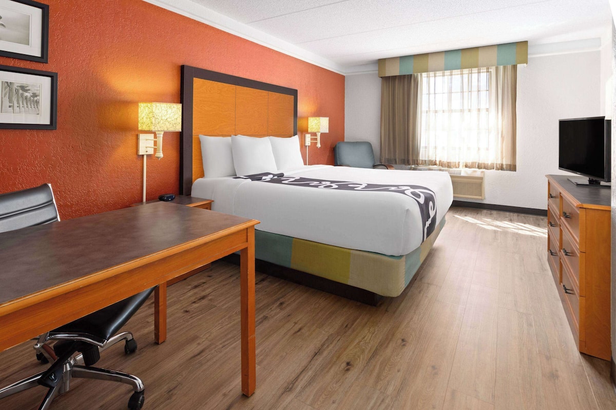 Une chambre d’hôtel équipée d’un lit, d’un bureau, d’une chaise, d’une télévision et d’une fenêtre avec des rideaux.