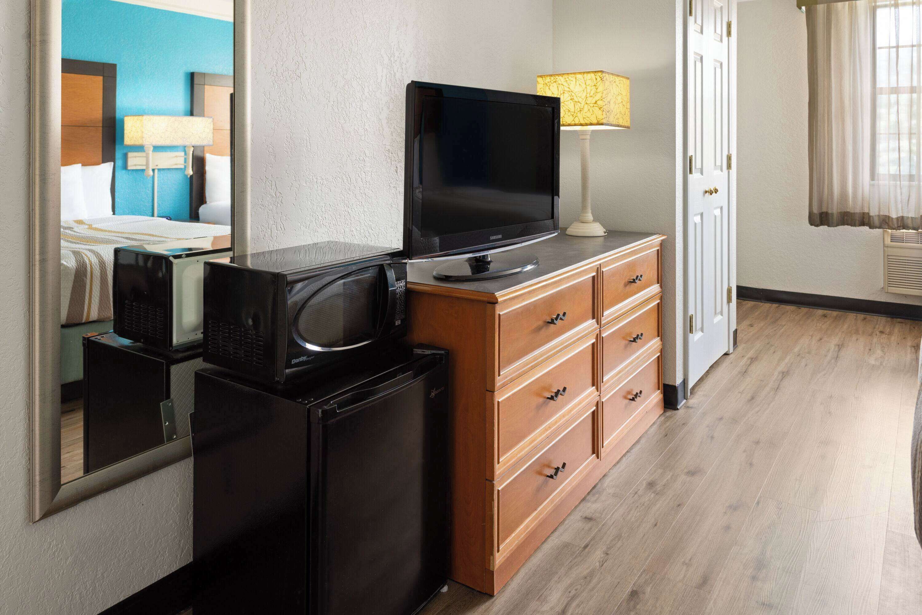 A hotel room with a television on a wooden dresser, a microwave, and a refrigerator.
