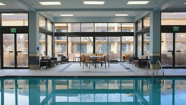 A pool area with a table and chairs, a pool ladder, and large windows. - Courtyard by Marriott Rockford (Rockford)