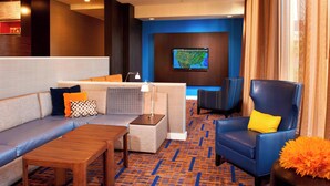 A modern hotel lobby with a sectional sofa, a blue armchair, a wooden coffee table, and a flat-screen TV mounted on the wall. - Courtyard by Marriott Rockford (Rockford)