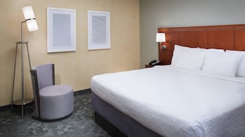 Habitación de hotel con una cama grande, una silla, dos obras de arte enmarcadas, una lámpara de pie y una mesita de noche con lámpara.