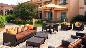 An outdoor patio area with wicker furniture, a table, and an umbrella. - Courtyard by Marriott Rockford (Rockford)