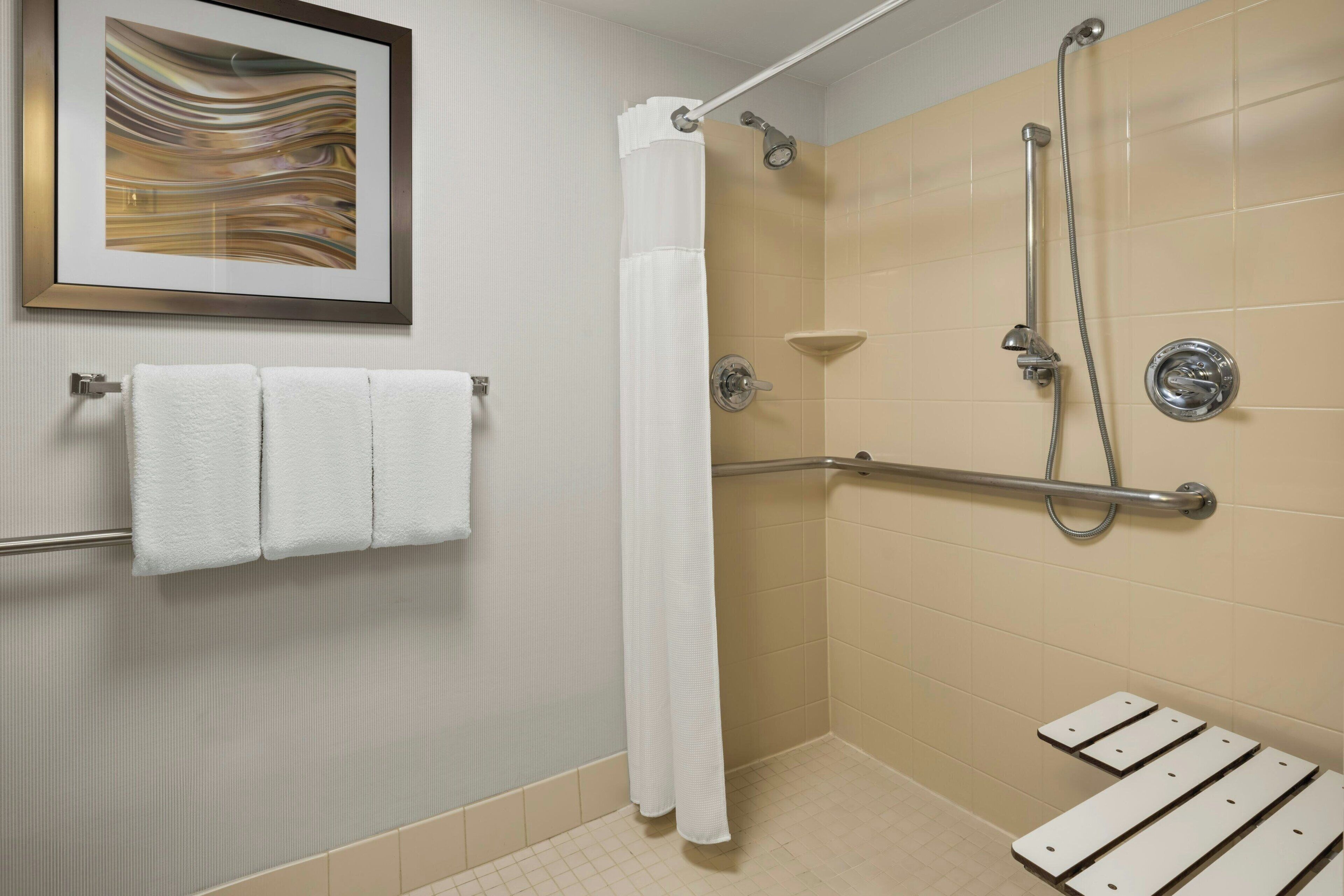A shower area with a handrail, a white shower curtain, and a framed artwork on the wall.