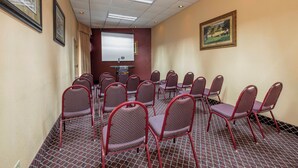 A conference room with rows of chairs, a projector screen, and a carpeted floor. - Red Roof Inn & Suites Macon (Macon)