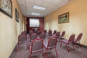 A conference room with rows of chairs, a projector screen, and a carpeted floor. - Red Roof Inn & Suites Macon (Macon)