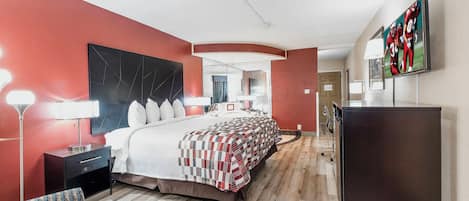 Una habitación de hotel con una cama grande, mesitas de noche, un escritorio, un televisor de pantalla plana y un espejo.