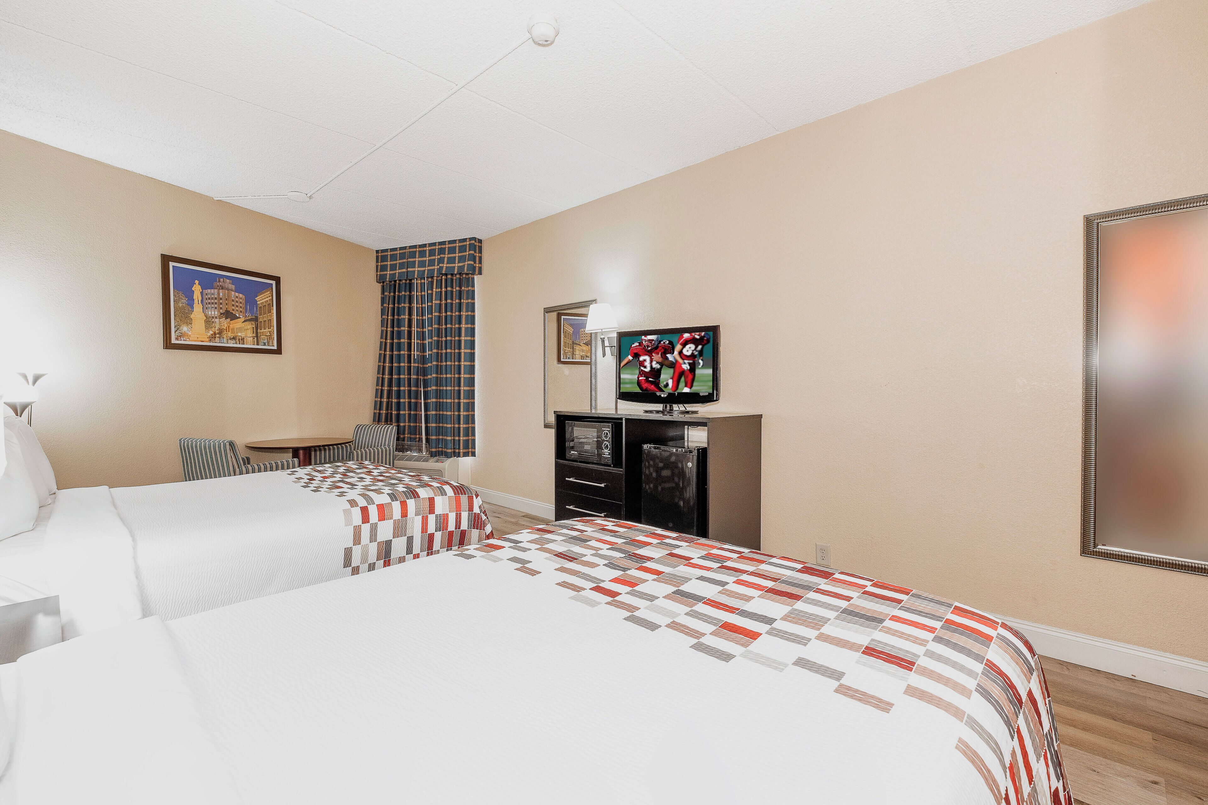 A hotel room with two beds, a television, a small table, and a window with curtains.