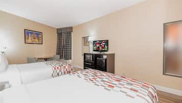 A hotel room with two beds, a television, a small table, and a window with curtains.