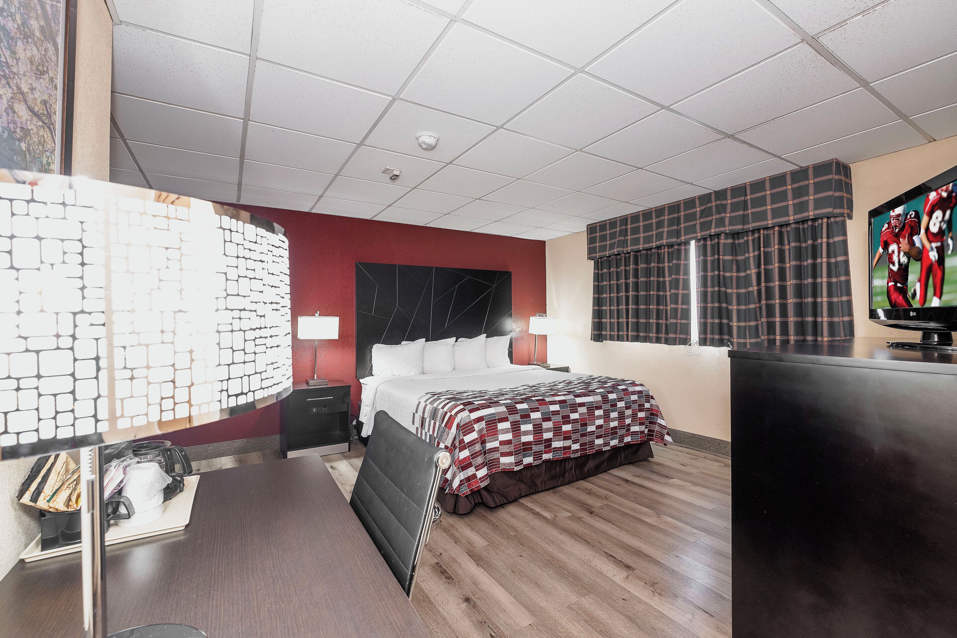 Een hotelkamer met een bed, een bureau, een televisietoestel en een raam met gordijnen.