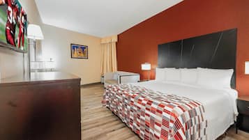 A hotel room with a bed, a desk, a chair, a lamp, and a painting on the wall.