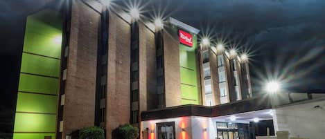 Un hôtel avec une enseigne rouge, de nombreuses fenêtres et un parking.