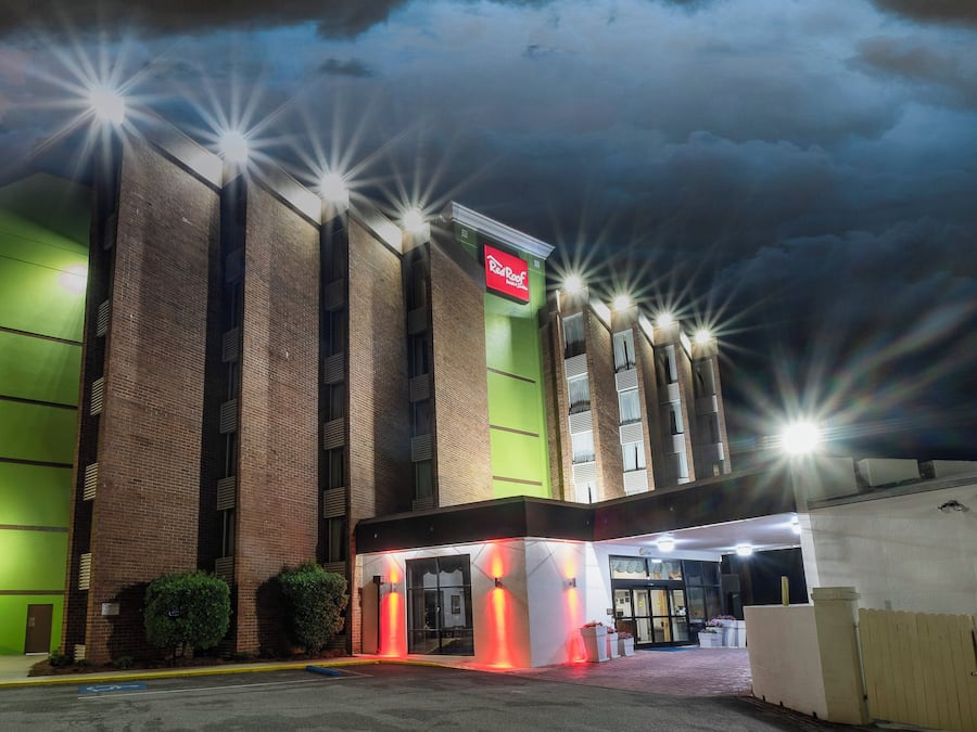 A hotel with a red sign, multiple windows, and a parking lot.