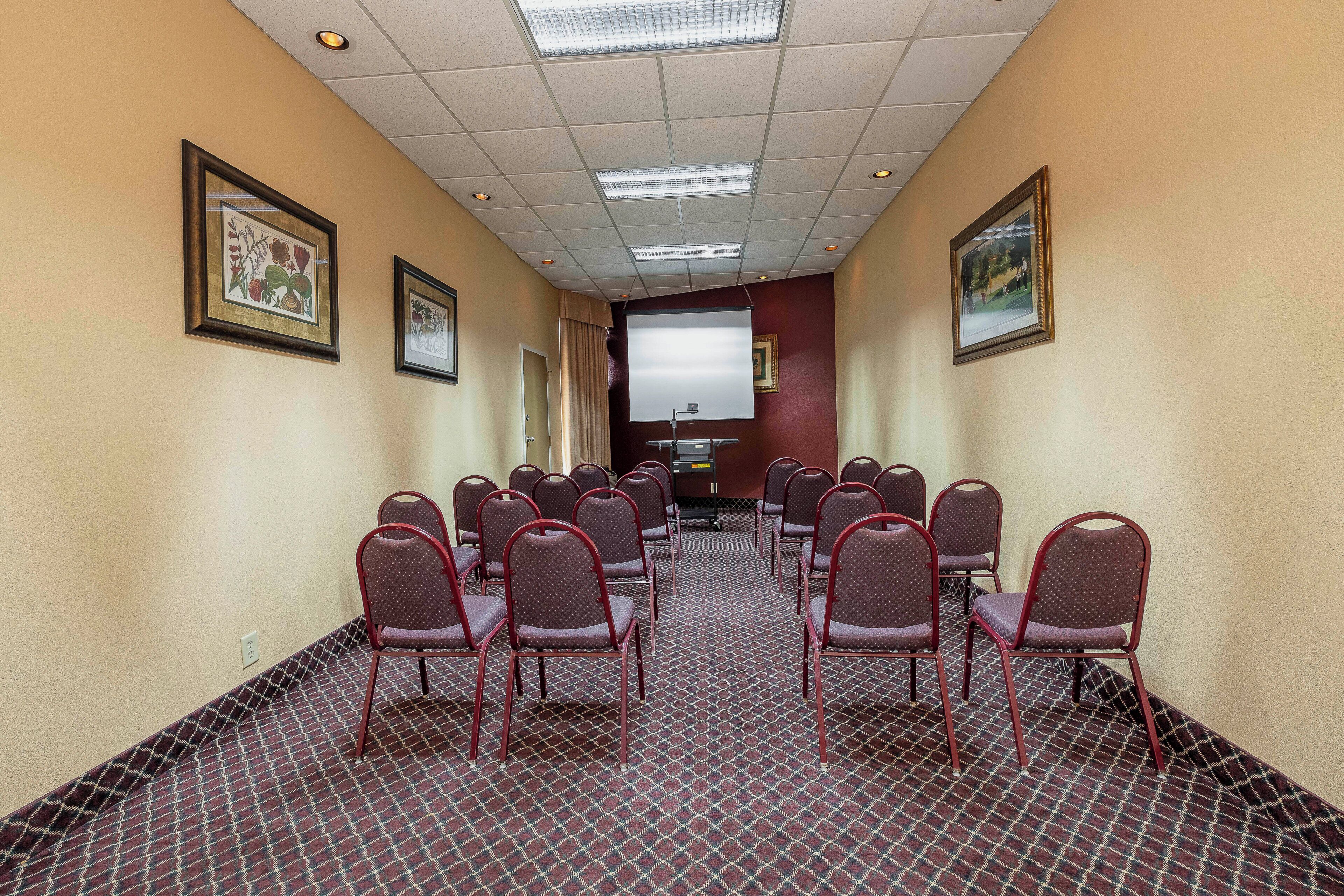 Un salón de conferencias con filas de sillas, una pantalla de proyector e impresiones botánicas enmarcadas en las paredes.