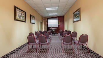 Un salón de conferencias con filas de sillas, una pantalla de proyector e impresiones botánicas enmarcadas en las paredes.