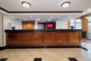 A reception desk with a flat-screen TV, wooden paneling, and a tiled floor. - Red Roof Inn & Suites Macon (Macon)