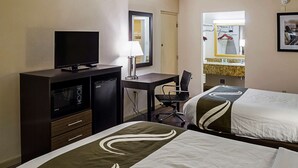 Ett hotellrum med två sängar, ett skrivbord med en tv, en skrivbordslampa, en stol och en spegel.