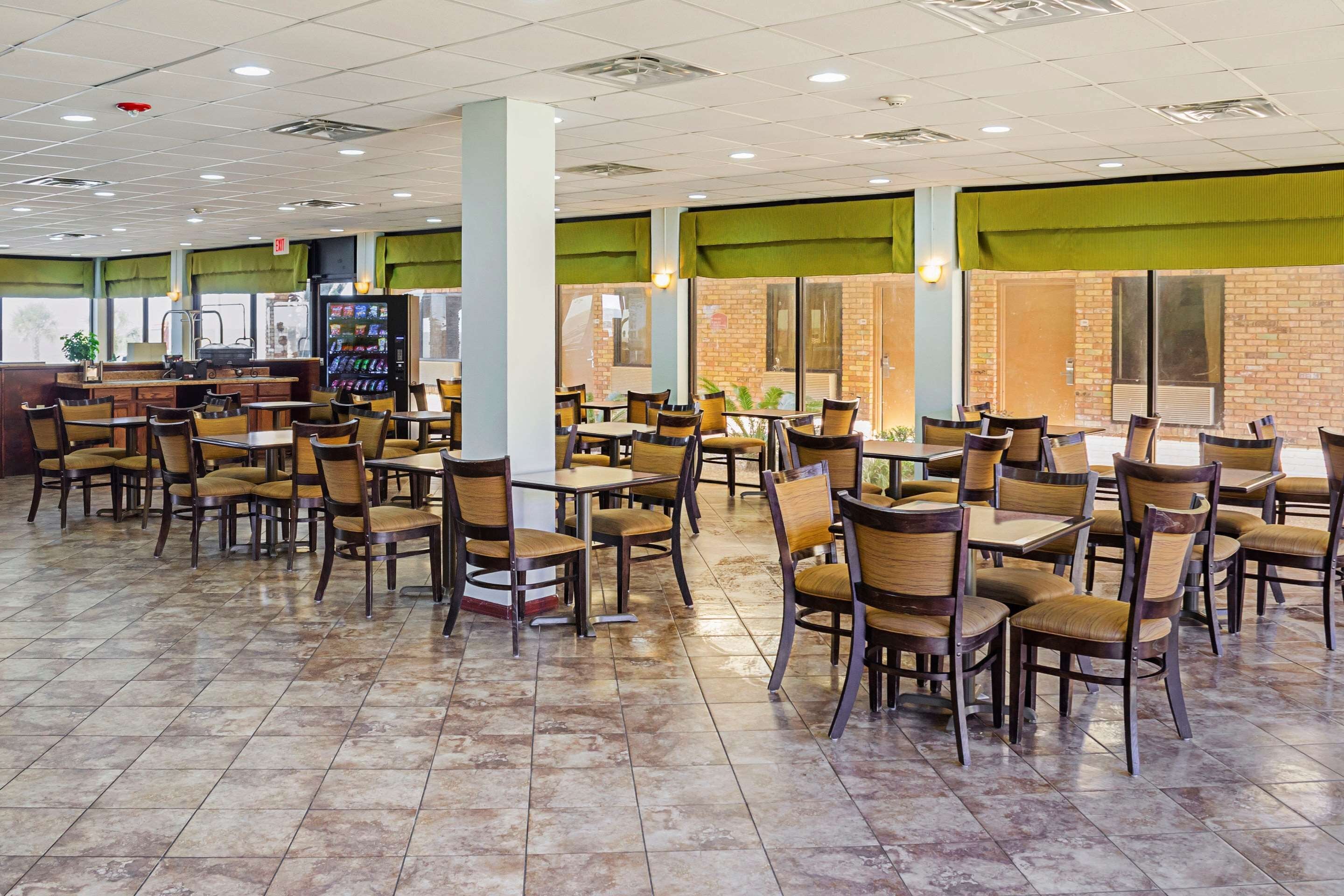 Un grand espace intérieur aménagé en salle à manger, avec plusieurs tables et chaises, un distributeur automatique et un mur en briques en arrière-plan.