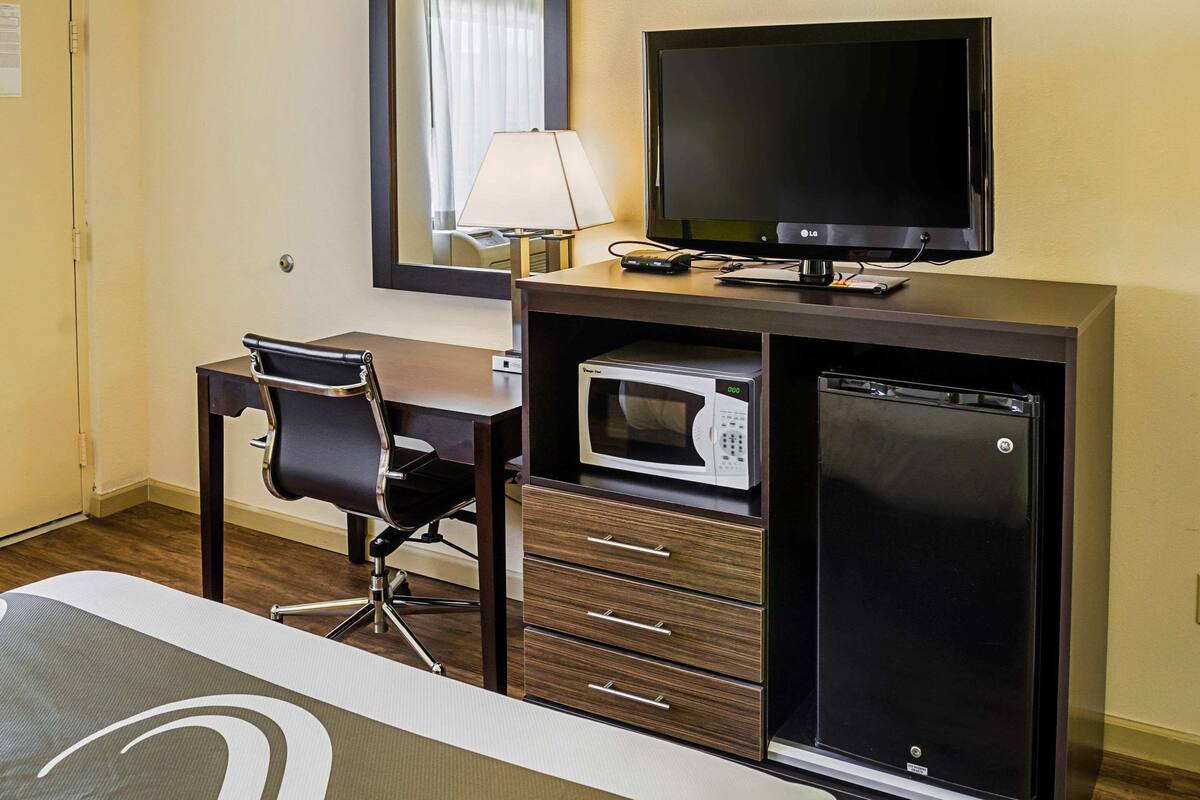 A hotel room with a desk, chair, television, microwave, and refrigerator.