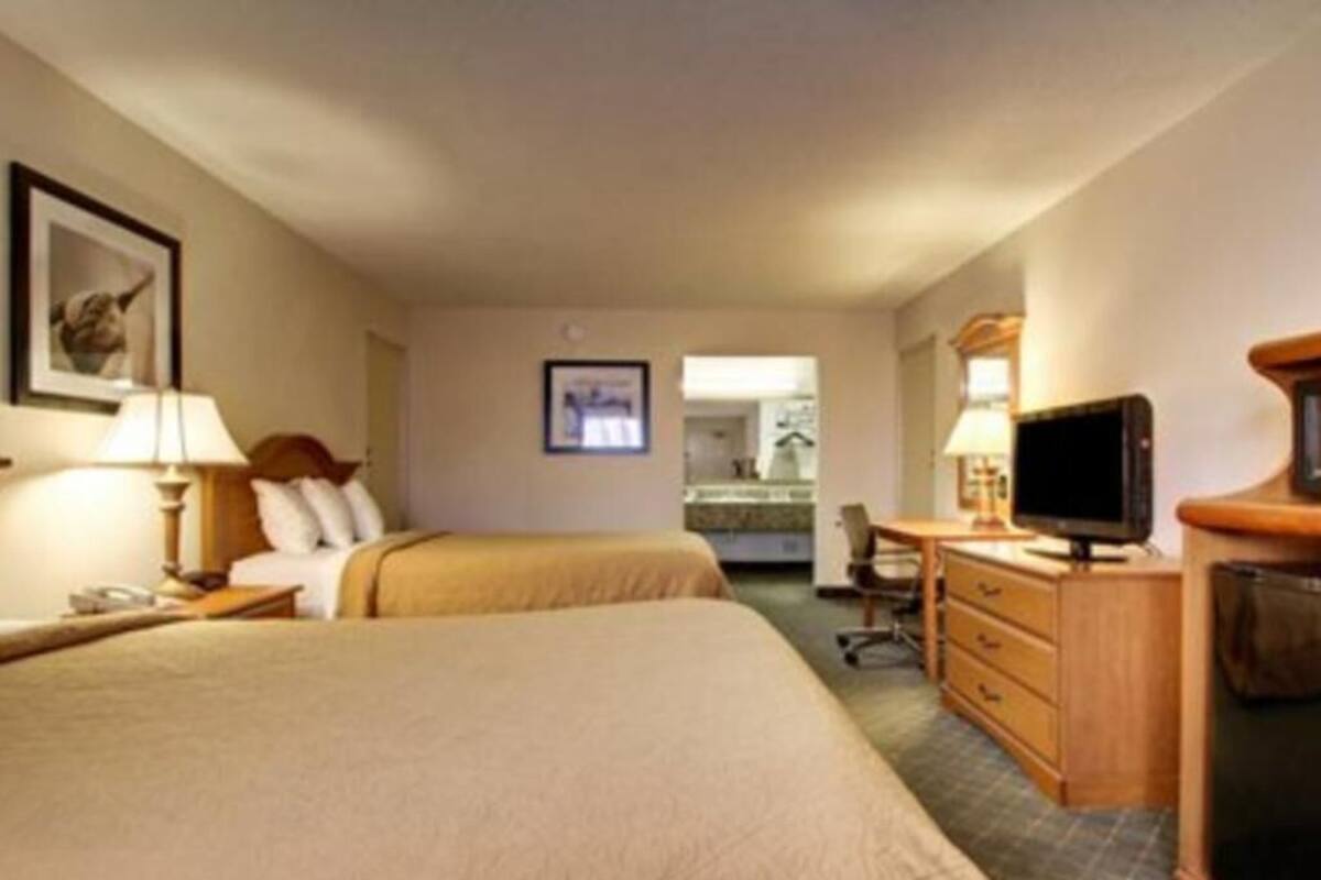 A hotel room with two beds, a desk with a television, and a chair.