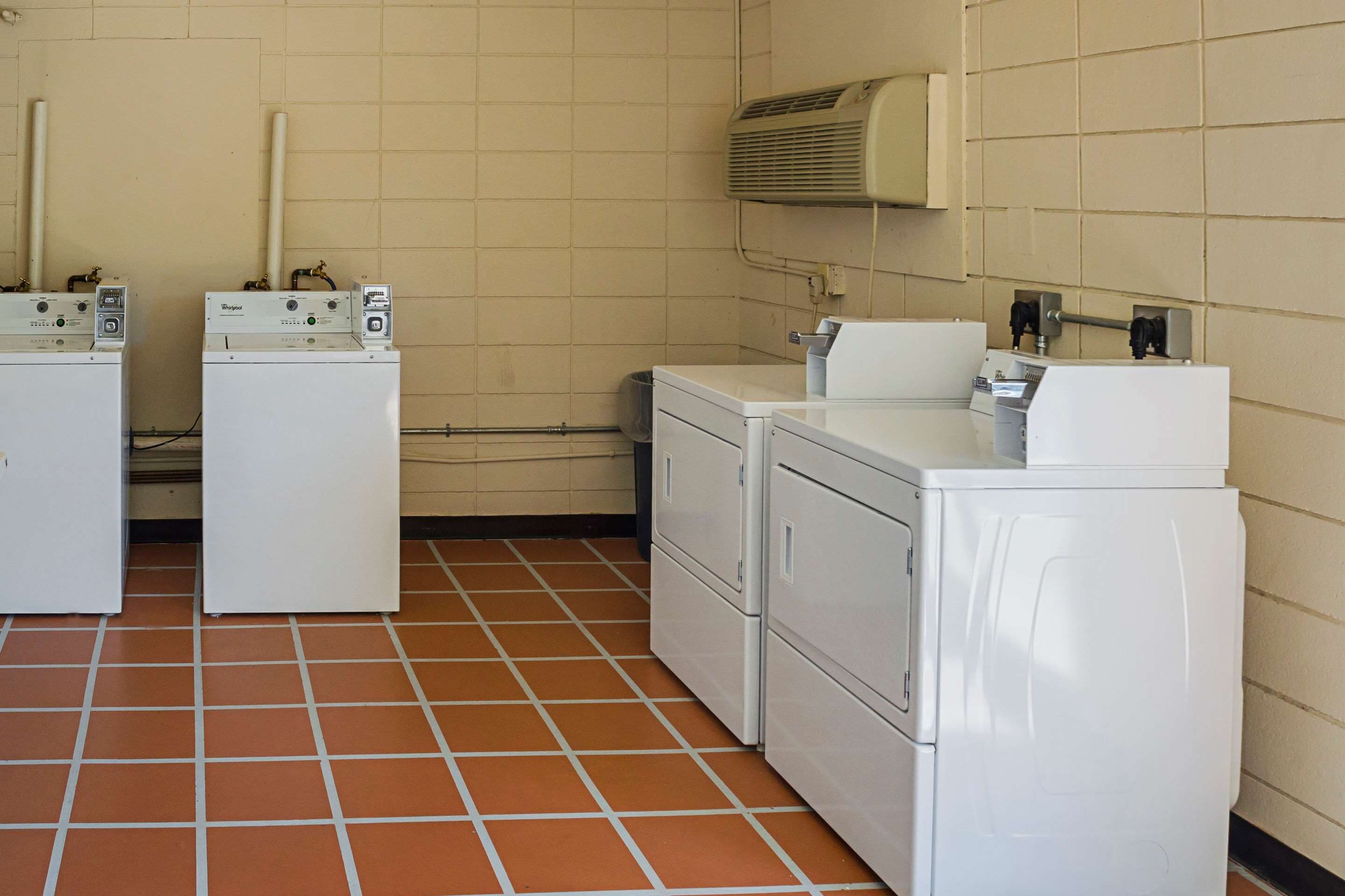 A laundry room with two front-loading washing machines, a dryer, and a wall-mounted air conditioner.