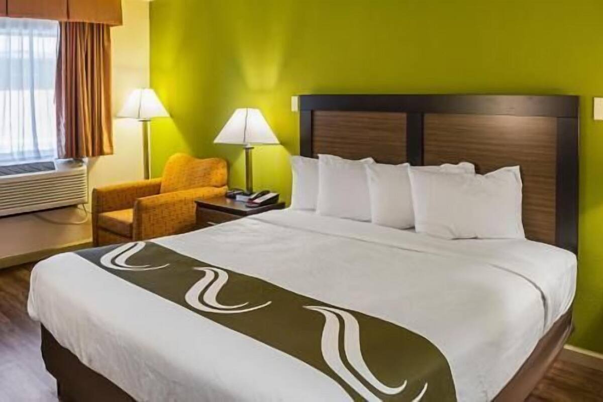 A hotel room with a bed, a chair, a lamp, and a nightstand.