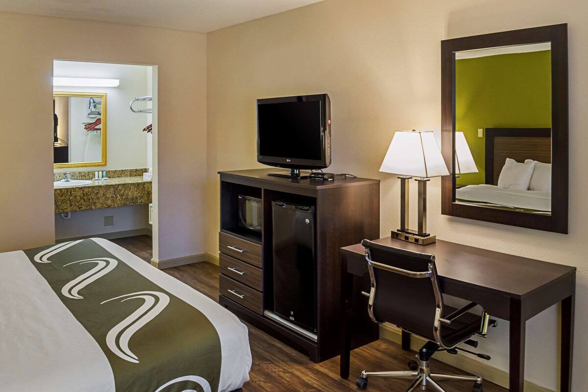 A hotel room with a bed, a desk with a computer, a television, and a mirror.