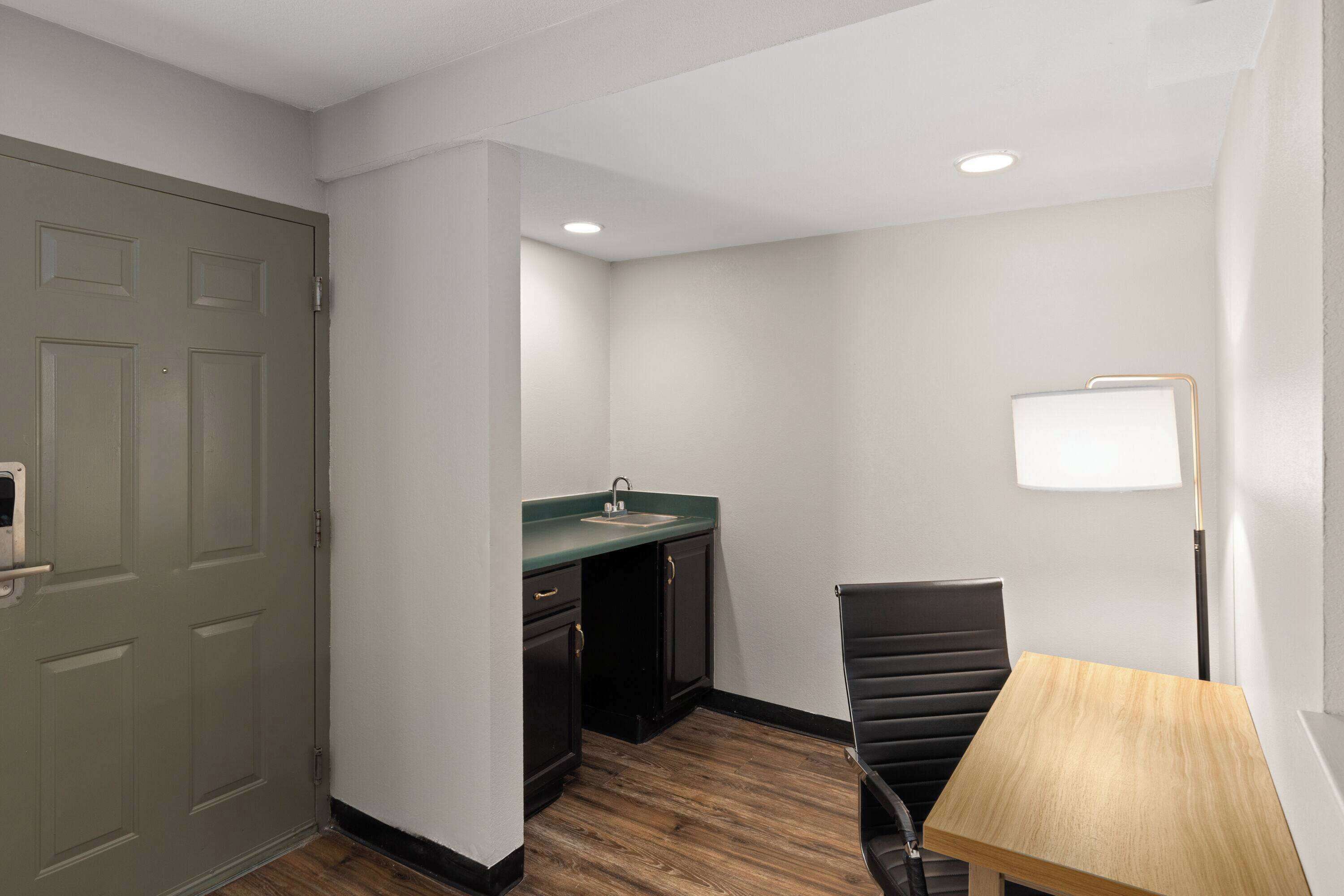 A small, clean room with a wooden floor, a green door, a sink, and a chair.