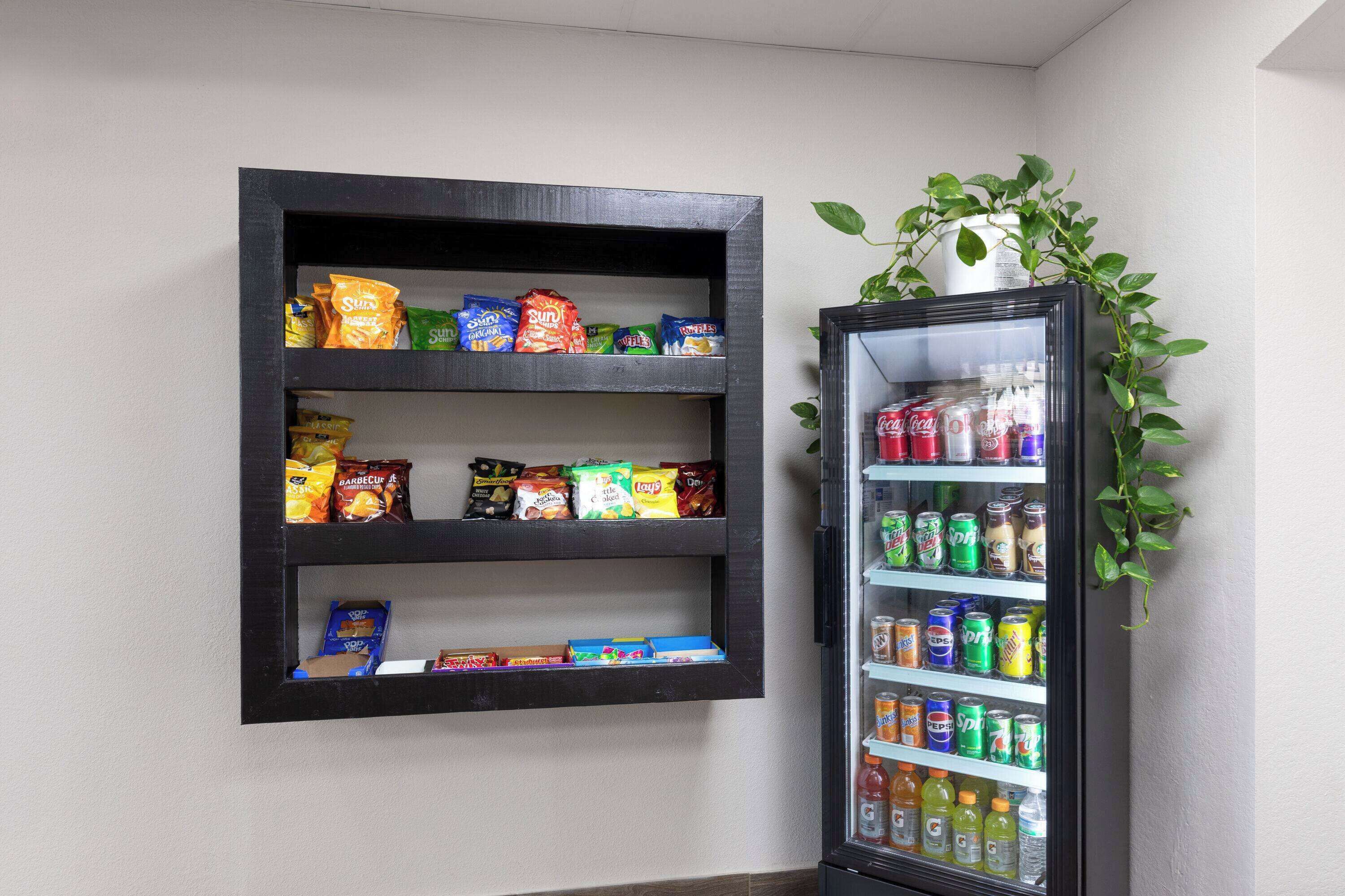 A wall-mounted snack shelf with various packaged snacks and a beverage refrigerator with multiple drink options.