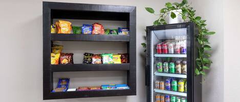 A wall-mounted snack shelf with various packaged snacks and a beverage refrigerator with multiple drink options.