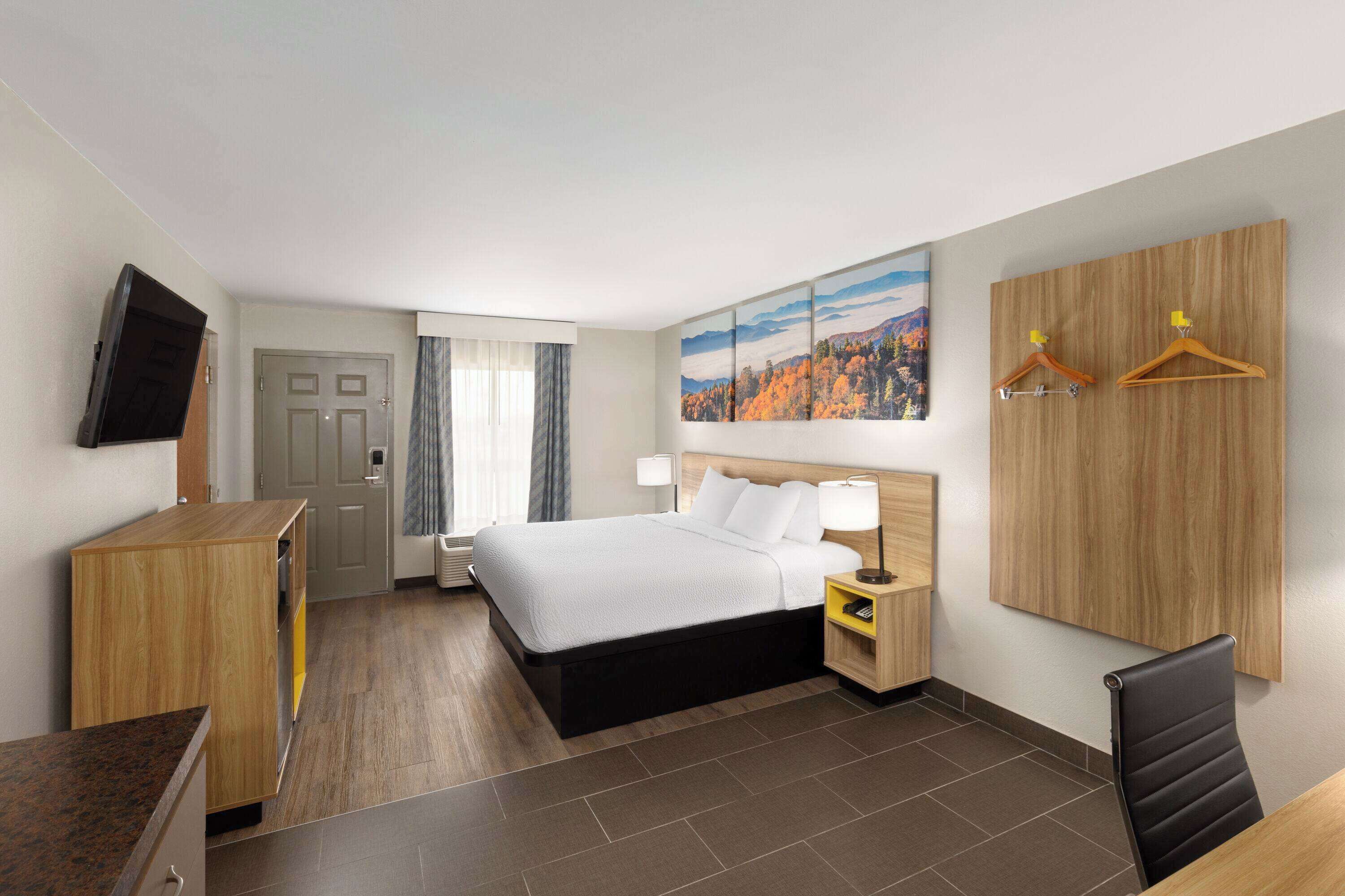 Een hotelkamer met een bed, nachtkastjes, een bureau, een televisie, een kledingkast en een schilderij aan de muur.