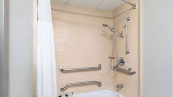 A bathroom with beige tiles, a white bathtub, and a shower with a handheld showerhead and grab bars.