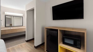 Una habitación de hotel moderna con televisión de pantalla plana montada en la pared, microondas integrado y un refrigerador pequeño.
